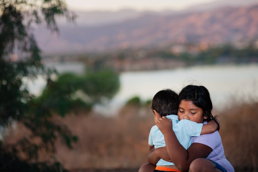 Brother and sister separated from parents are hugging each other in a foreign country, across a river.